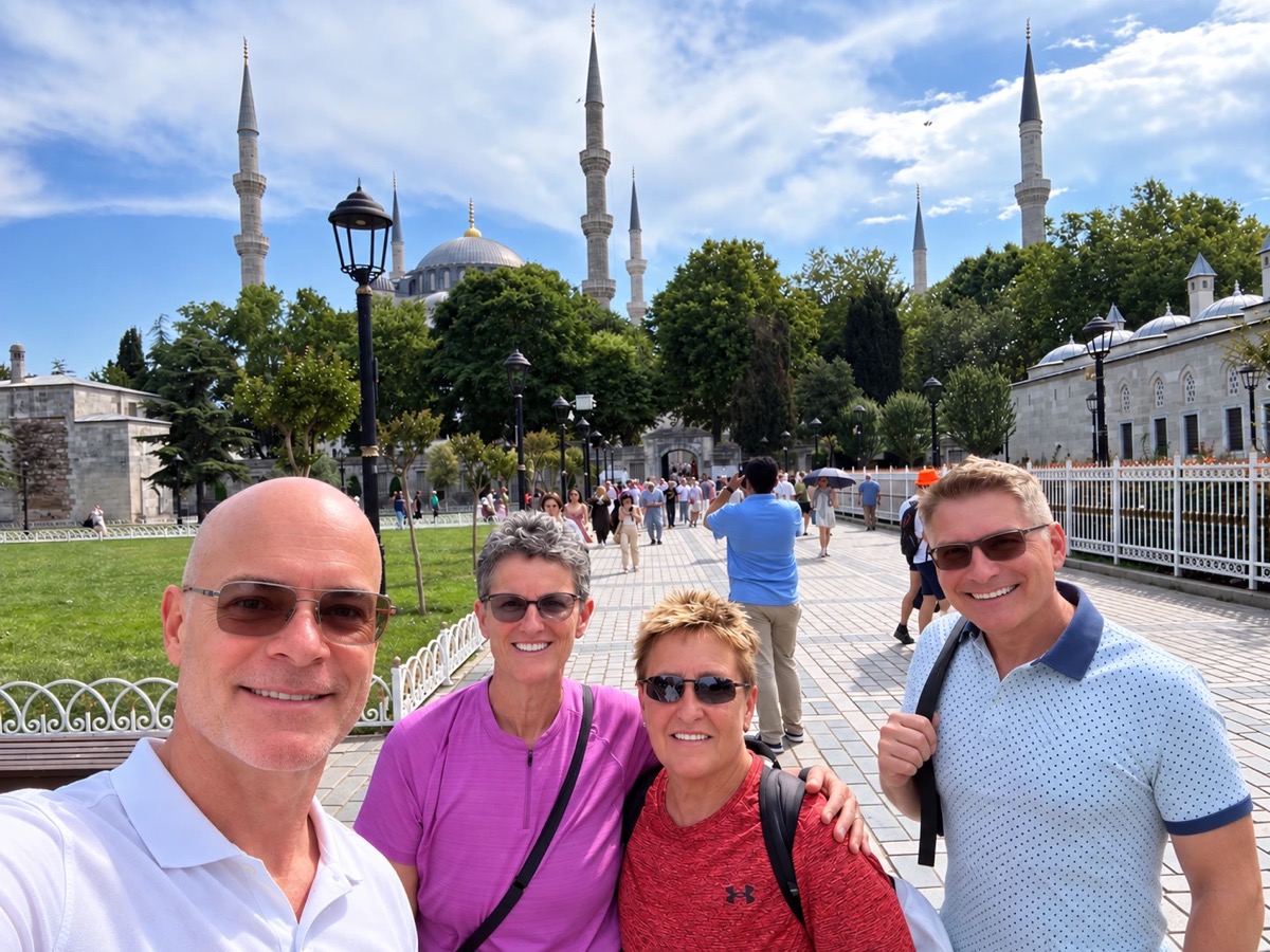 Four people smiling in a selfie on a sunny plaza, with the domes and minarets of the Blue Mosque behind them.