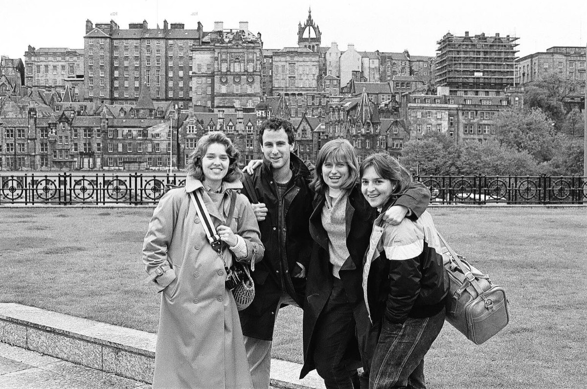 Four students in the gardens below Princes Street with the Old Town and the crown spire of St Giles' behind them.