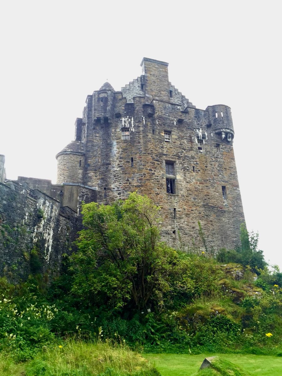 The stone tower of Eilean Donan Castle under a white sky, seen from below.