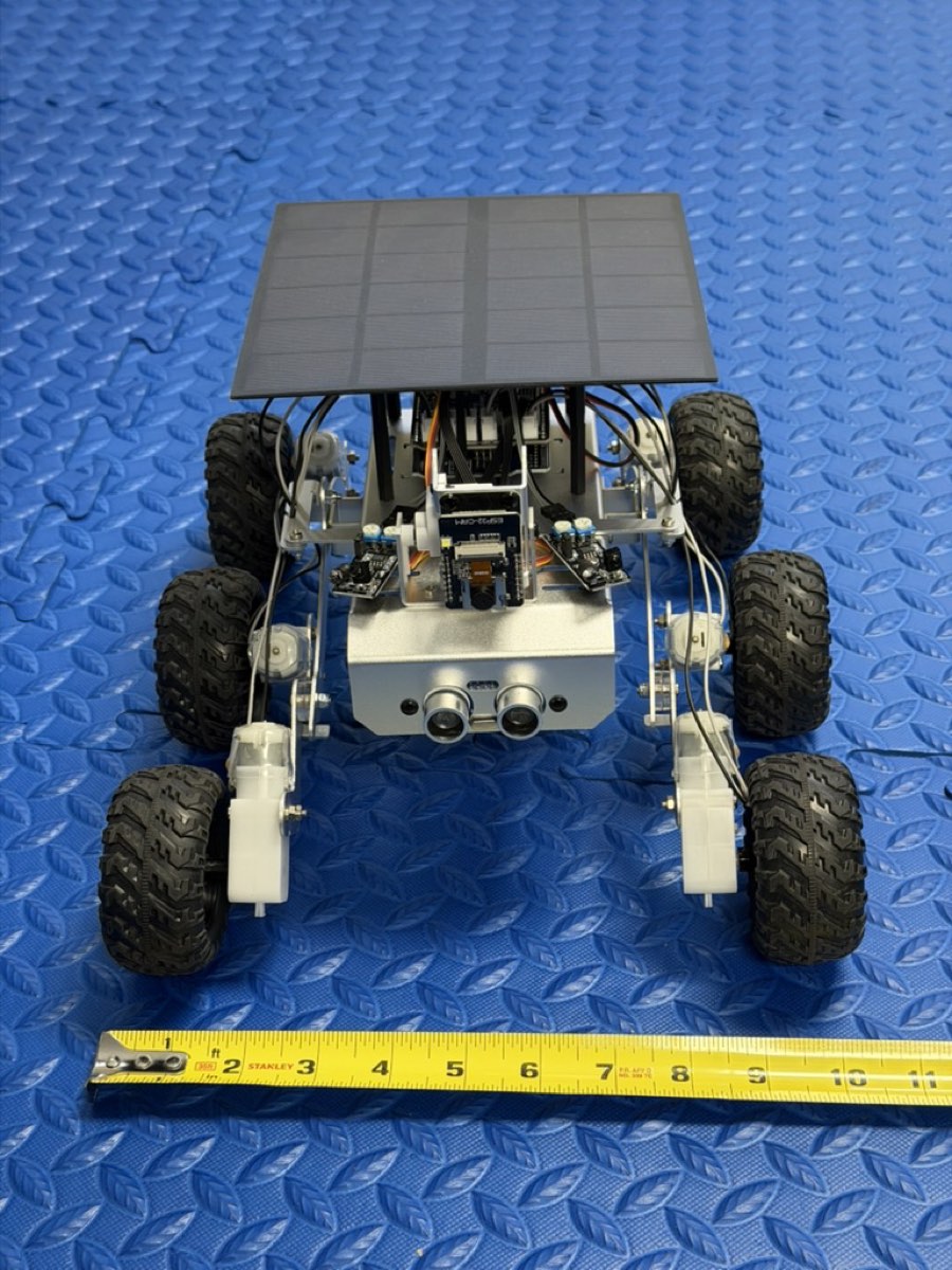 The rover from the front with a tape measure laid across the mat in front of it reading about ten inches.